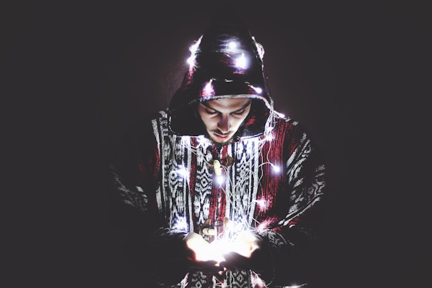 Close-up of a black oversized hoodie with vivid neon purple embroidered fantasy motifs glowing softly under dim light.