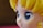 A close-up view of a stylized character figure with large, glossy blue eyes. The figure has yellow hair styled in distinct waves and a smooth complexion typical of anime or cartoon characters.