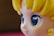 A close-up view of a stylized character figure with large, glossy blue eyes. The figure has yellow hair styled in distinct waves and a smooth complexion typical of anime or cartoon characters.
