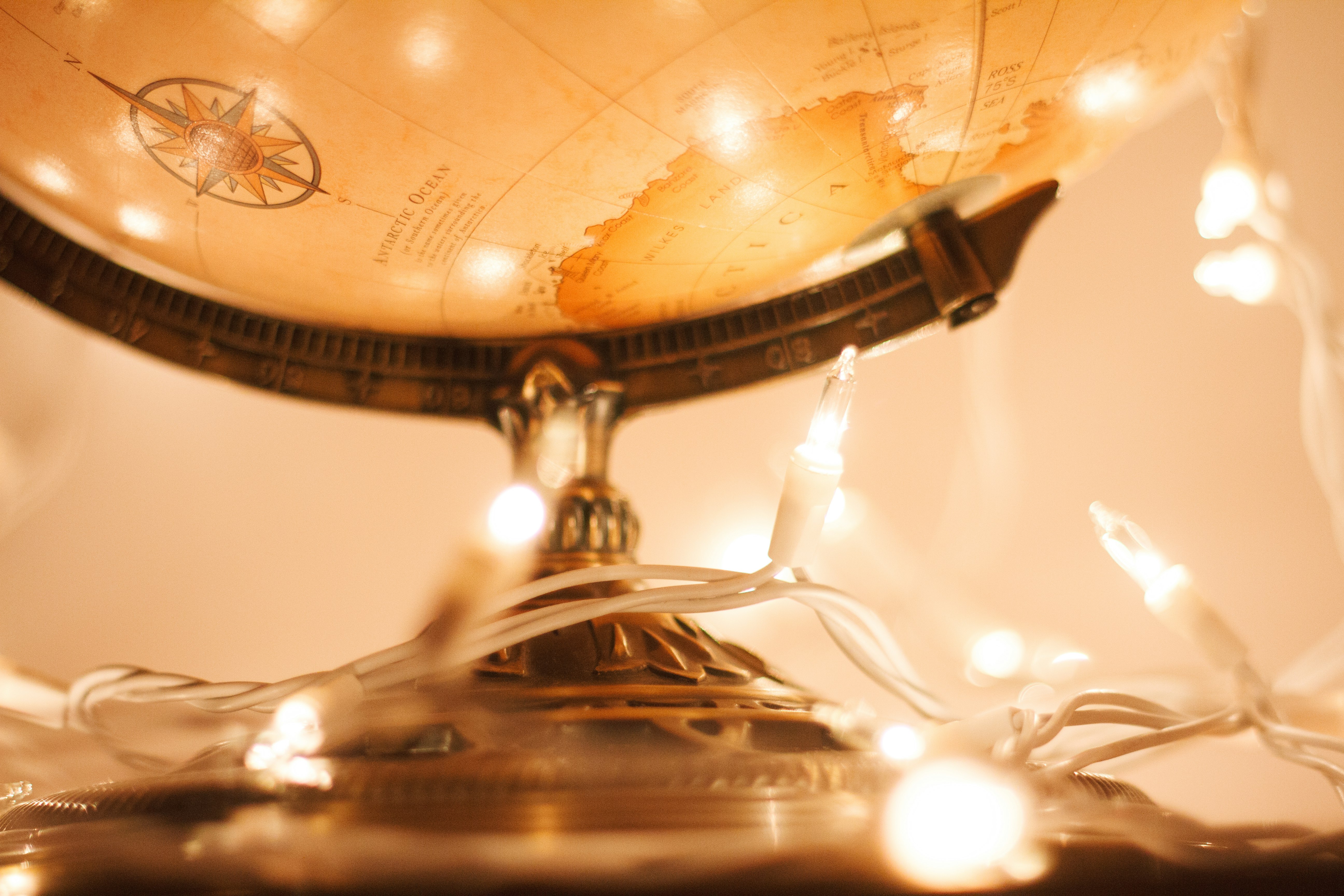 An antique globe is partially illuminated by a warm glow of white string lights that wrap around its base, creating an inviting and cozy ambiance. The globe's bronze stand adds a touch of vintage elegance.