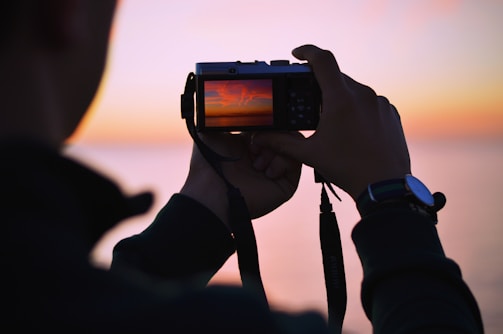 A beginner photographer capturing a vibrant sunset with a simple camera.