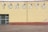 A brick wall with faded yellow paint features the large, block letters spelling out 'TORONTO'. Above the letters are a series of industrial lights. Several patches of paint appear chipped or weathered, and a small section of street pavement is visible in front of the wall.