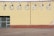 A brick wall with faded yellow paint features the large, block letters spelling out 'TORONTO'. Above the letters are a series of industrial lights. Several patches of paint appear chipped or weathered, and a small section of street pavement is visible in front of the wall.
