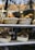 A bakery display window showcases two baskets filled with freshly baked bread at the top shelf and two loaves of dark, round bread in rectangular paper trays on the middle shelf. The warm tones of the bread contrast with the cool reflections on the glass.