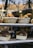 A bakery display window showcases two baskets filled with freshly baked bread at the top shelf and two loaves of dark, round bread in rectangular paper trays on the middle shelf. The warm tones of the bread contrast with the cool reflections on the glass.