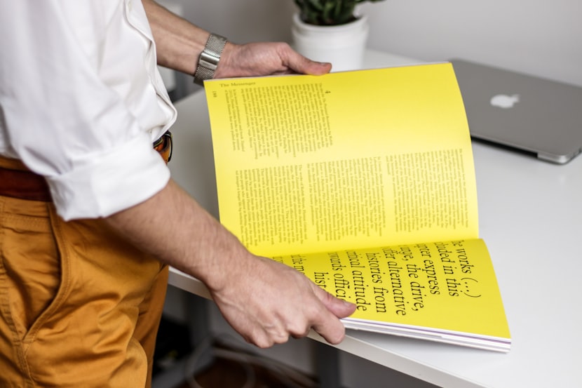 A man in a white shirt opening a book with yellow pages