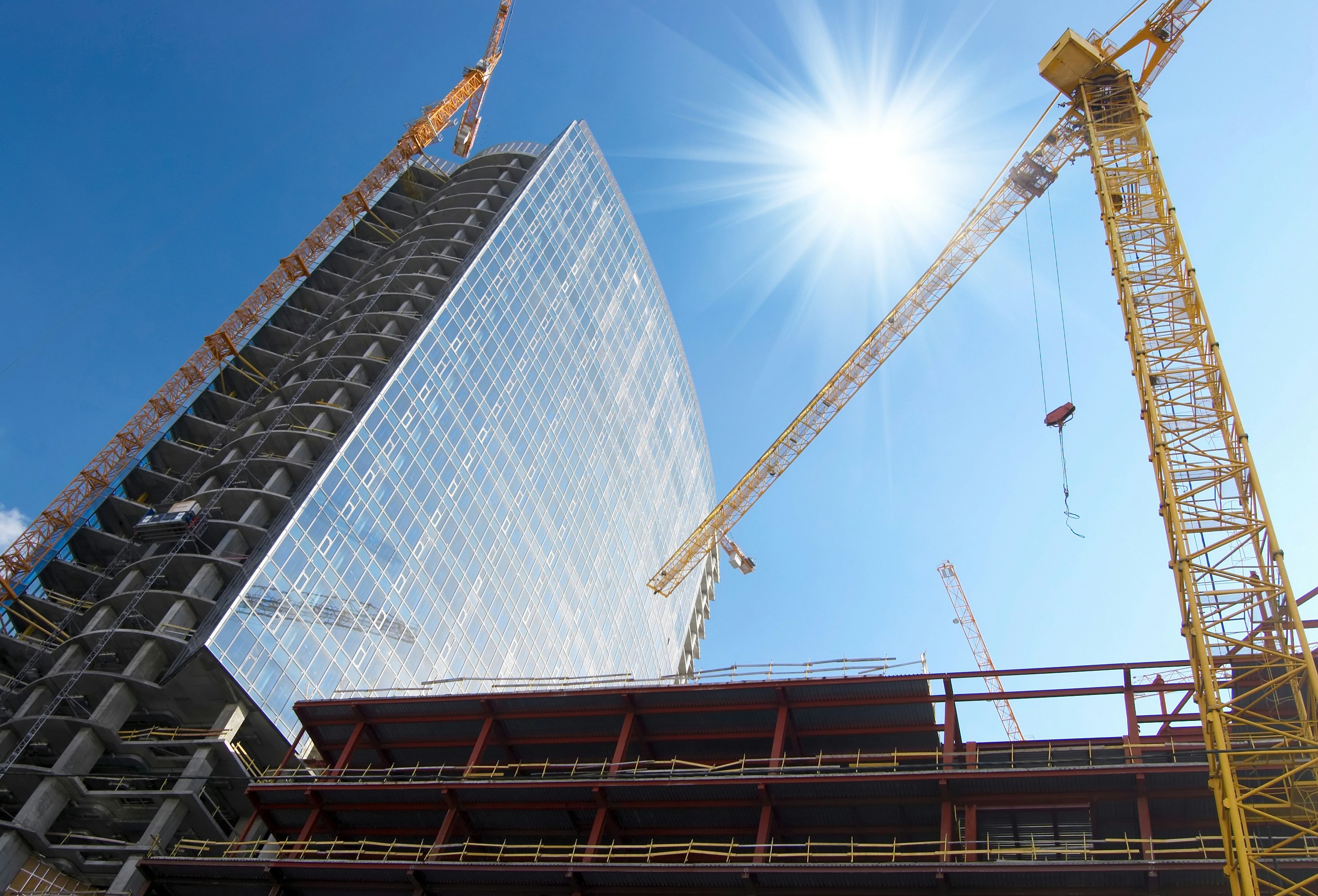 A modern apartment building under construction with cranes against a clear blue sky.