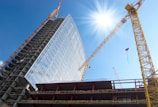 A panoramic view of a modern skyscraper under construction with cranes and workers.