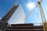 A sprawling commercial building under construction with cranes and scaffolding against a clear blue sky.