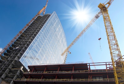 A construction site with cranes and workers building a modern structure under clear skies.