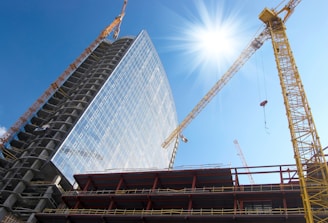 A modern high-rise building under construction with cranes and scaffolding against a clear blue sky.