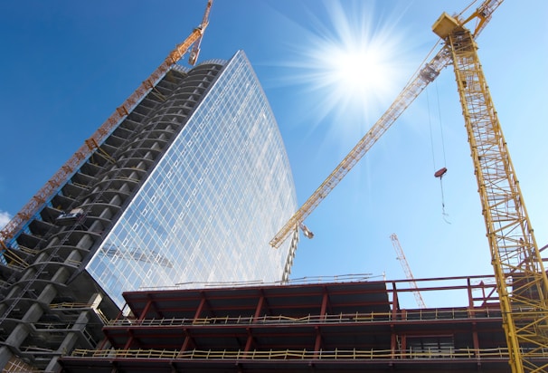 A modern high-rise building under construction with cranes against a clear blue sky.