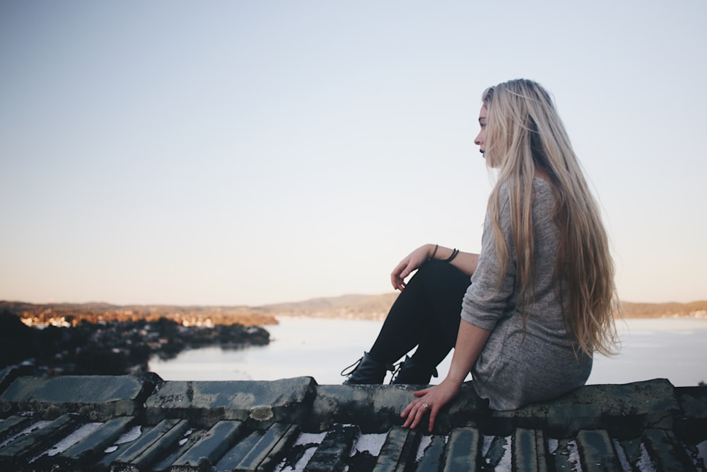 Femme assise sur le quai gris près de bpdy de l’eau