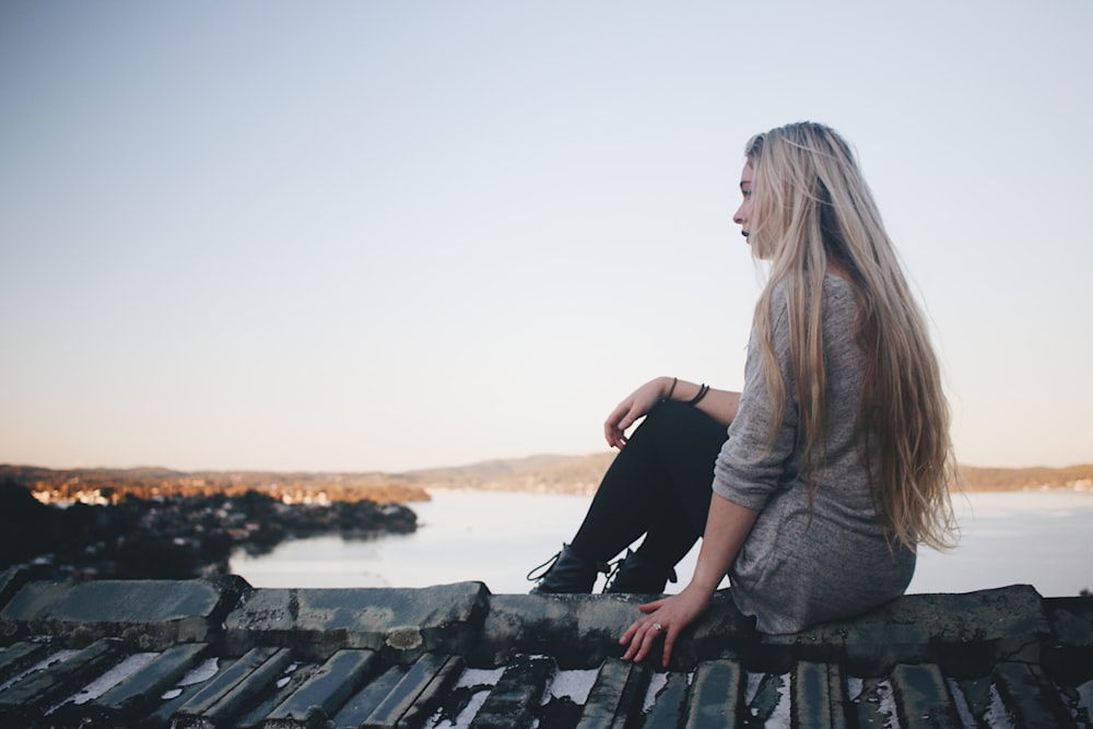 woman sitting on gray dock near bpdy of water