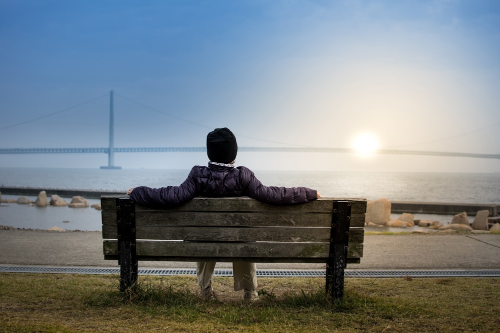 personne assise sur un banc face à un pont suspendu