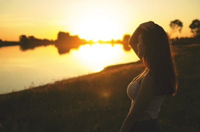 A serene woman meditating by a tranquil lake at sunset.