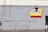 A gray concrete wall with several electrical boxes and conduits. A colorful sign hangs on the wall with a vinyl record graphic and the text 'Tower District Records' along with the words 'Buy Sell Trade Listen' in red. There is a small, partially visible door on the right side.