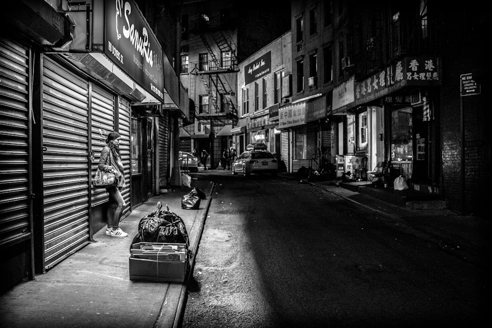 grayscale photography of woman standing infront of store shutter door at night