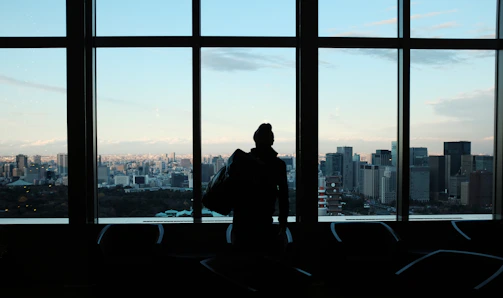 Silhouette of a male entrepreneur standing in a sleek modern office overlooking a cityscape at dusk.