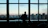 A focused woman reviewing documents with a city skyline visible through large office windows.
