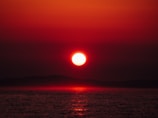 A vibrant red sky at dawn over a calm sea, reflecting warm hues.
