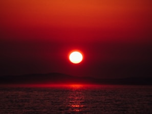 A vibrant red sky at dawn over a calm sea, reflecting warm hues.