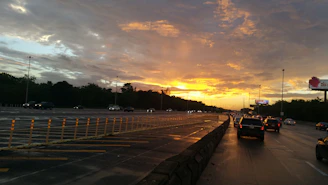 A large digital billboard towering over a busy highway with cars streaming beneath it during sunset.