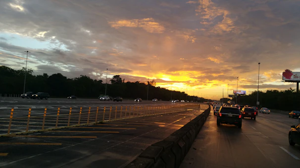 A large digital billboard towering over a busy highway with cars streaming beneath it during sunset.