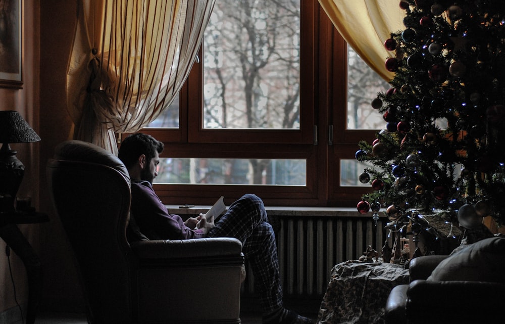 クリスマスツリーのそばのソファの椅子に座っている男性