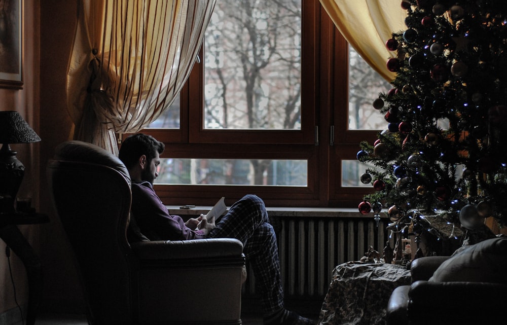 homme assis sur une chaise de canapé près de l’arbre de Noël