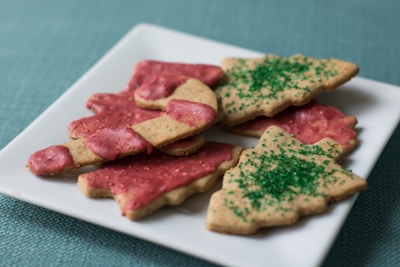 A white plate holds festive cookies shaped like Christmas trees. Some have pink frosting and others are sprinkled with green sugar.
