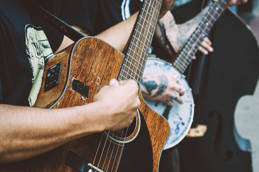 A close-up of a man's hand clutching a pick and playing a worn-out acoustic guitar