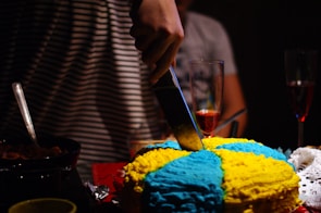 Close-up of hands cutting a beautifully decorated birthday cake surrounded by smiling guests.
