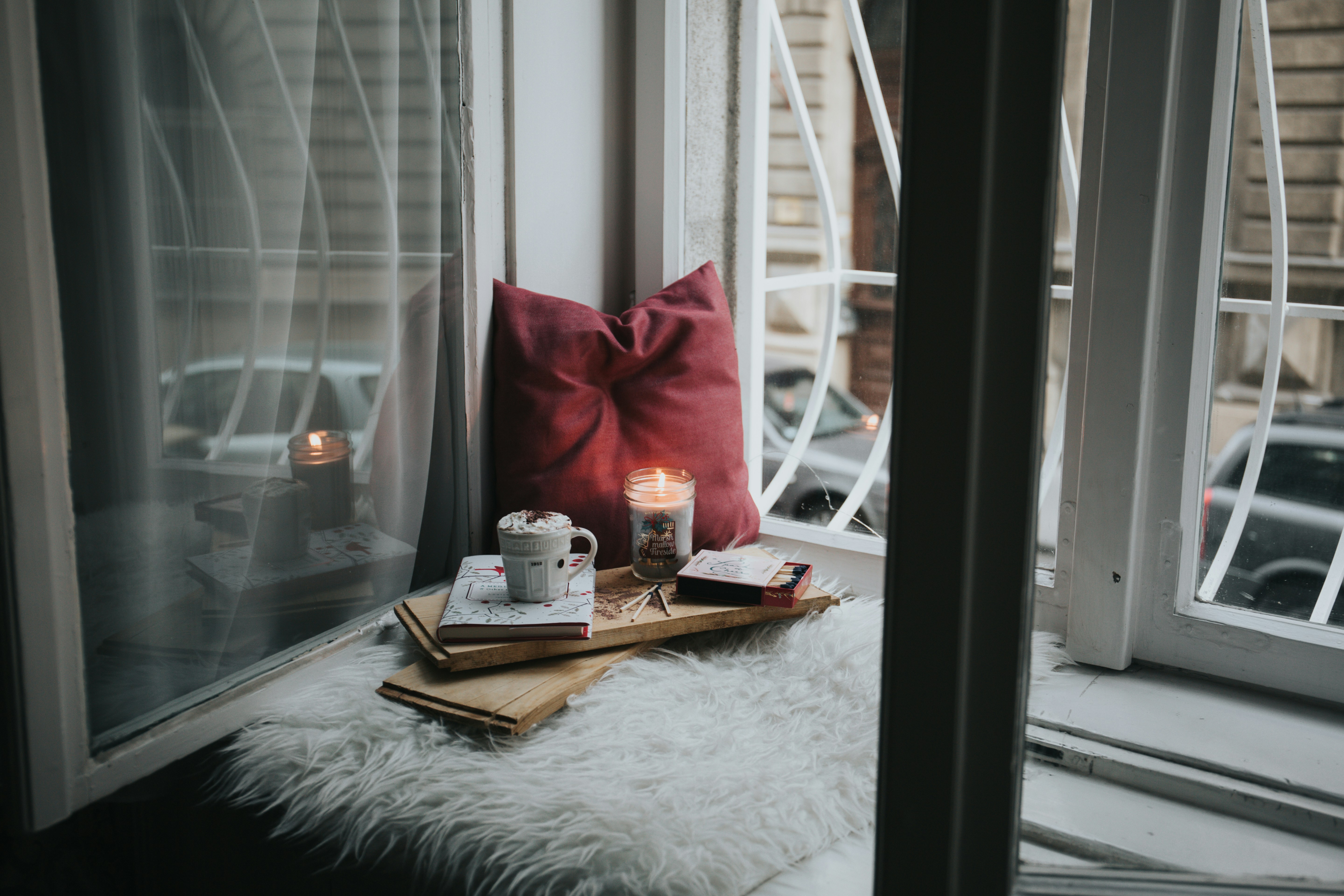 An example of a self-care kit, with a pillow, some books, a candle, and a mug topped with whipped cream set on a windowsill.