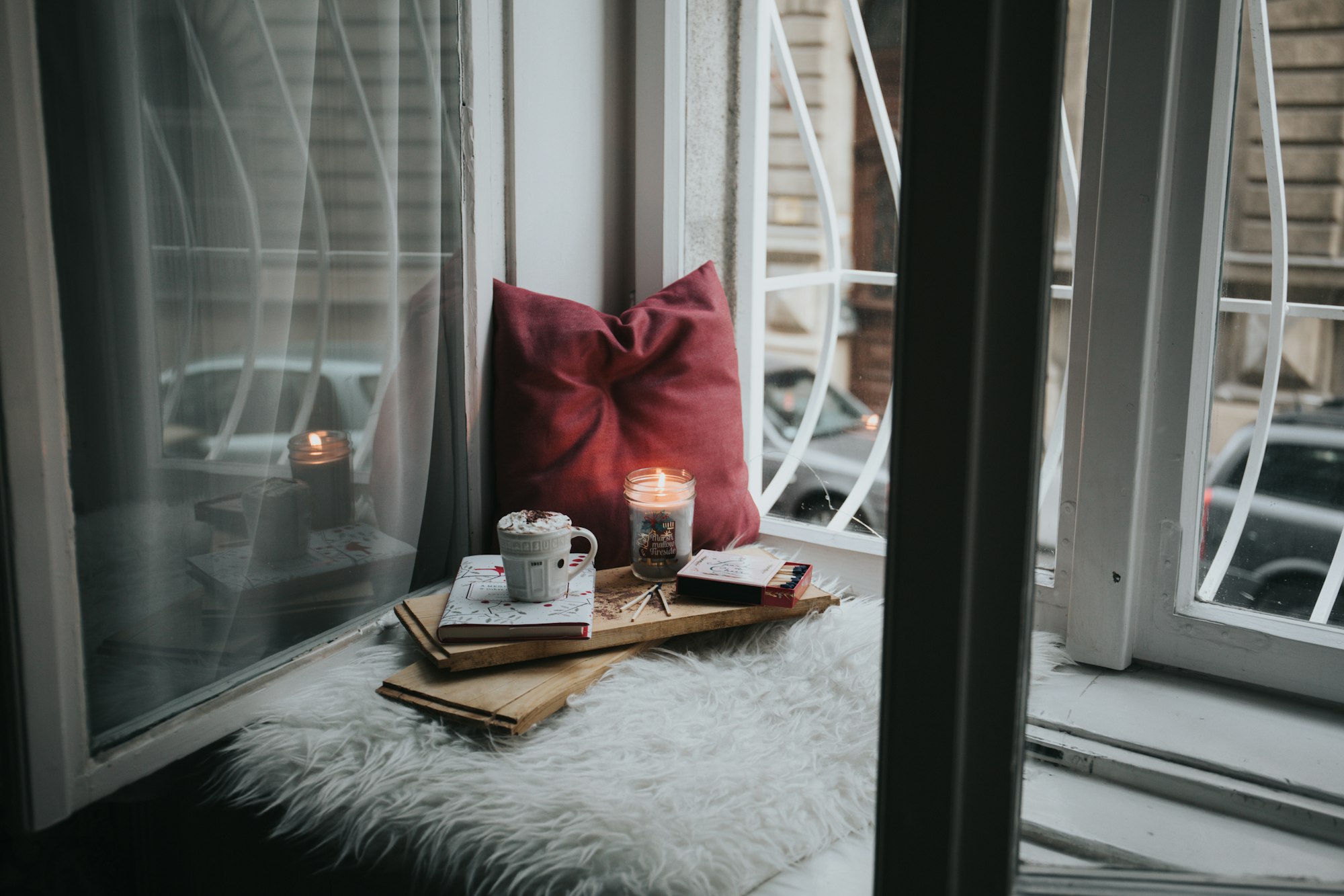 photo of candle on board beside pillow in a reading nook