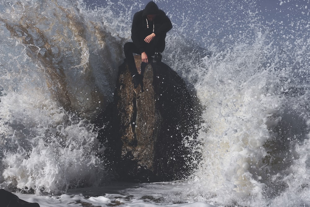 uomo che si siede sulla pietra in mezzo al mare d'ondeggiamento