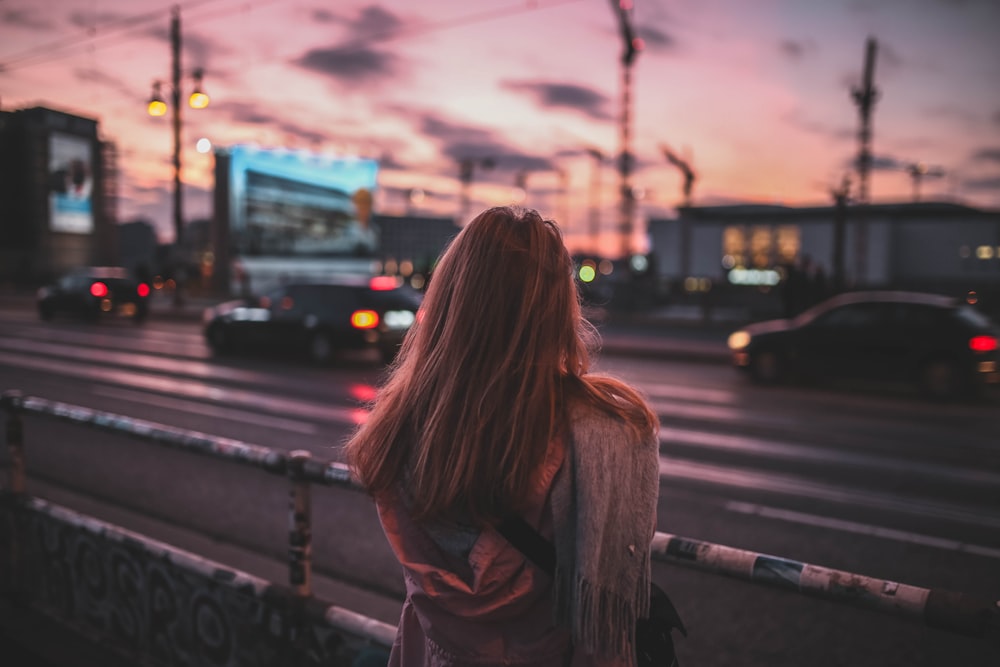 woman standing on rail facing road at dusk