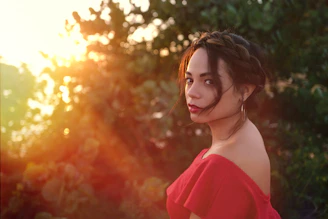A lifestyle shot of a woman enjoying a sunny day, wearing a flowing red dress and gold accessories from xo éclat.