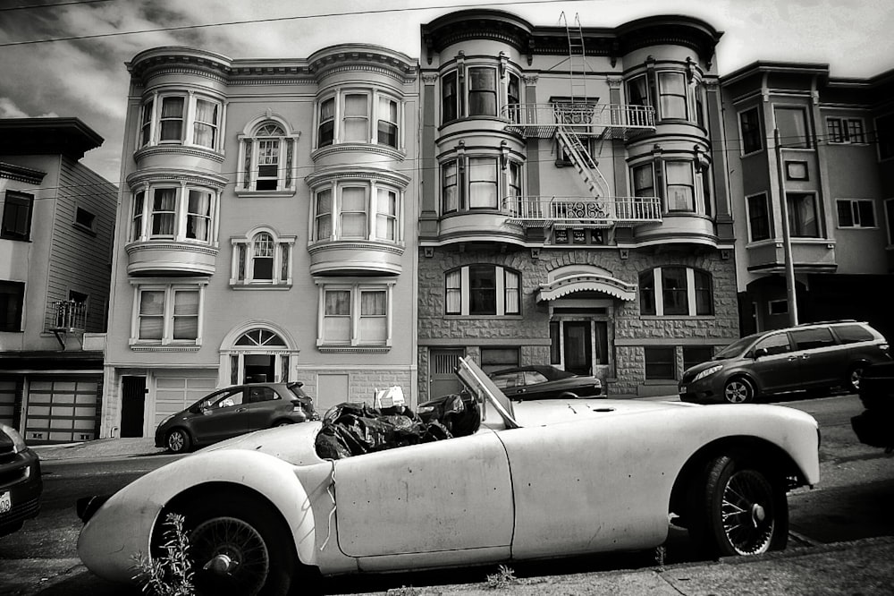 grayscale photo of convertible coupe park near building
