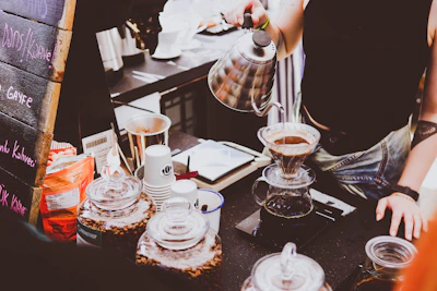 A barista preparing coffee with a pour-over method, showing steam rising from a freshly brewed cup.