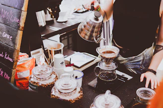 A barista preparing coffee with a pour-over method, showing steam rising from a freshly brewed cup.