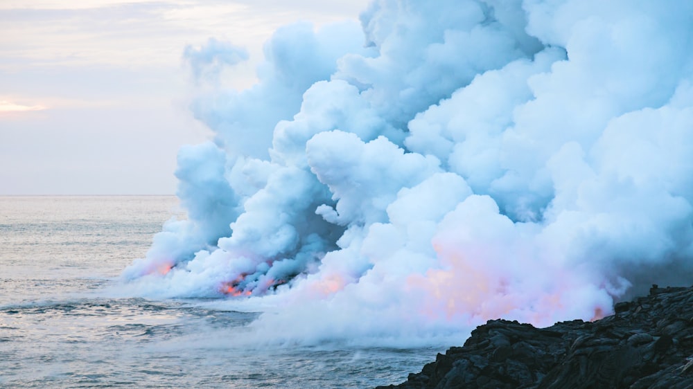 fire and smoke on body of water near rock formation under cloudy sky