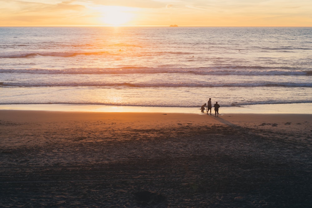 Fotografia dell'ora d'oro di tre persone sulla spiaggia