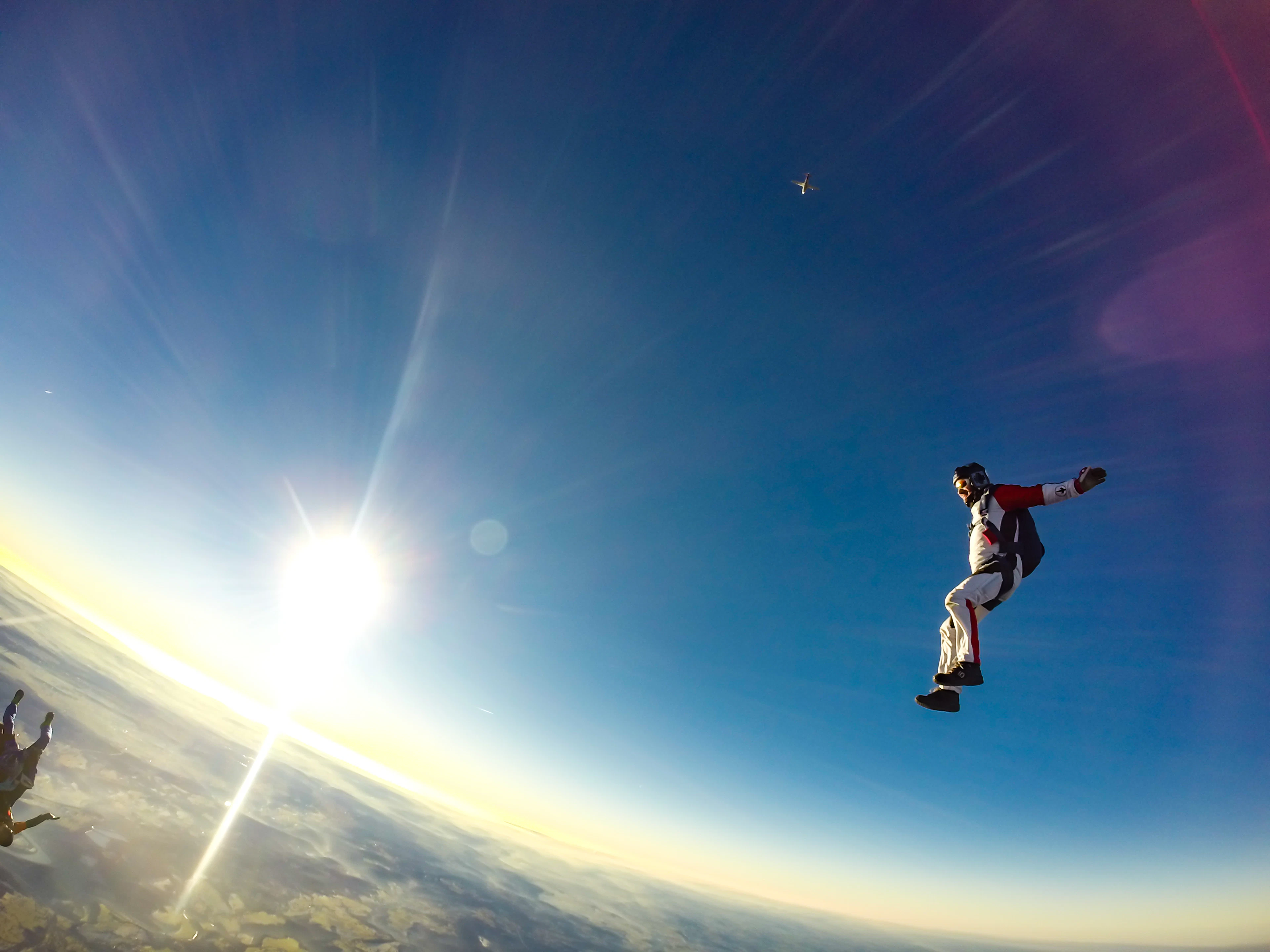 A skydiver in freefall high above the earth, lit by the low sun