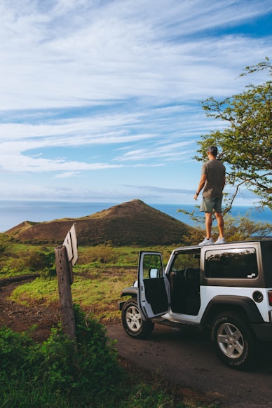man standing on roof of Jeep Wrangler parked on dirt road