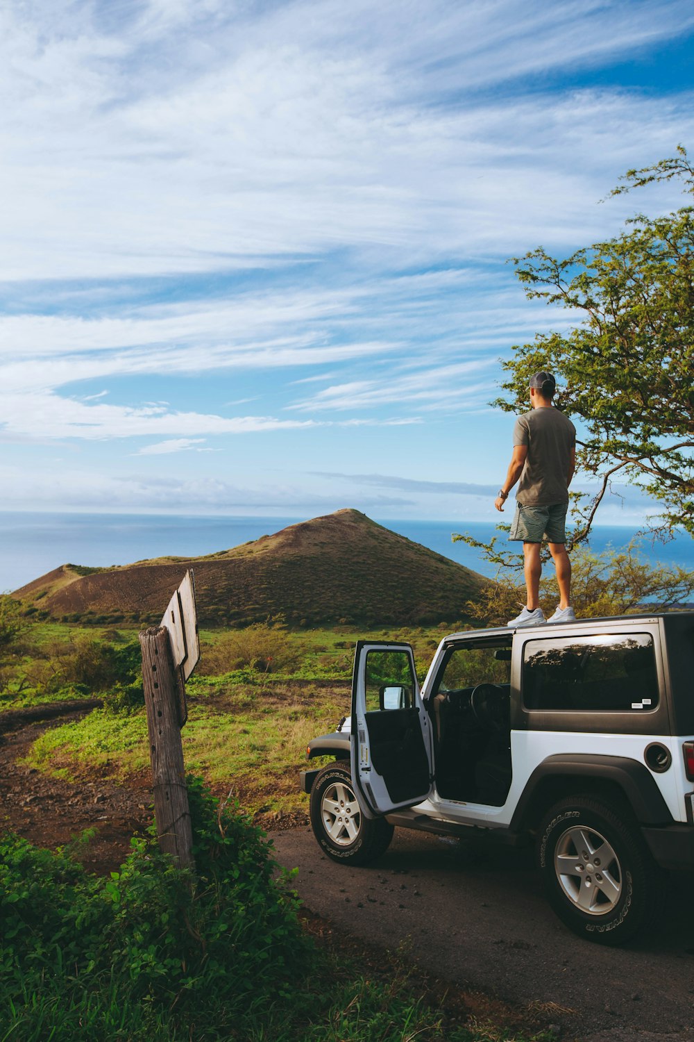 man standing on roof of Jeep Wrangler parked on dirt road