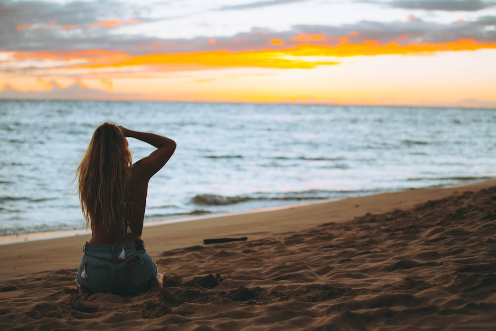 Mujer sentada en la orilla del mar mirando al mar durante la hora dorada