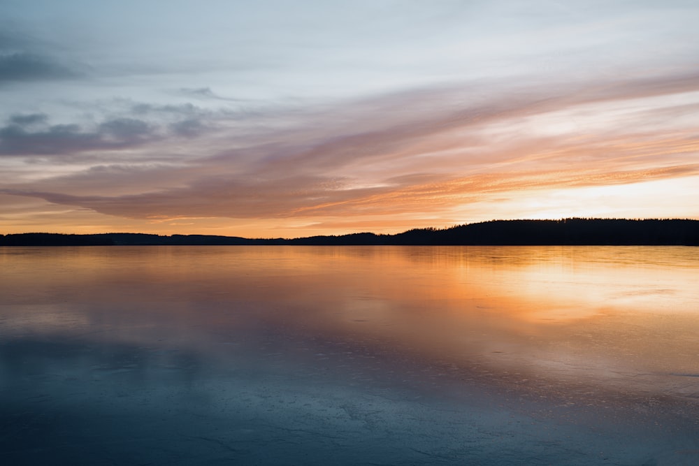 calm body of water near mountain during golden hour