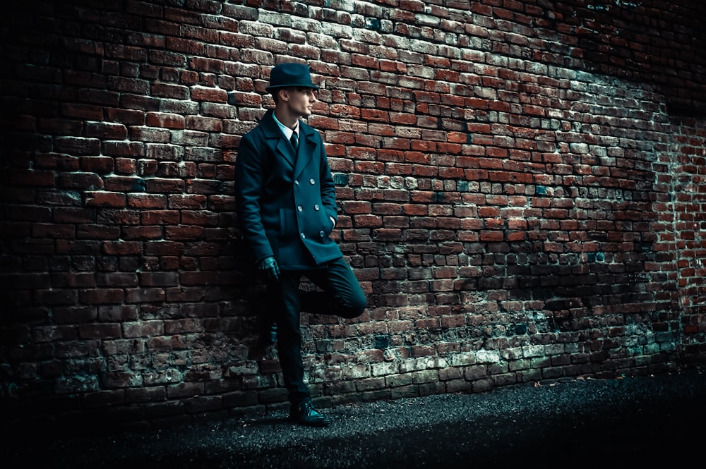 man wearing black coat leaning on brown brick wall