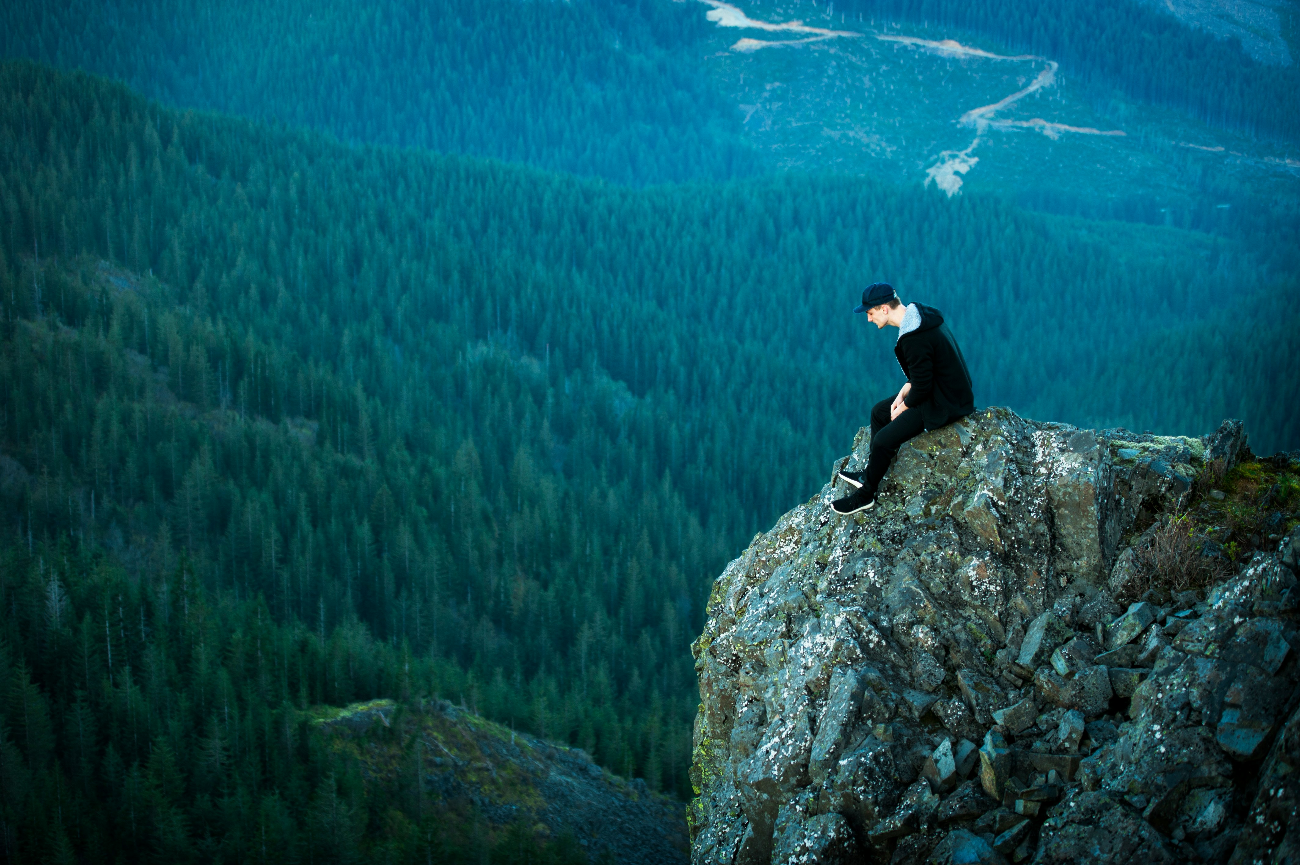 aerial view photography on man sitting on cliff